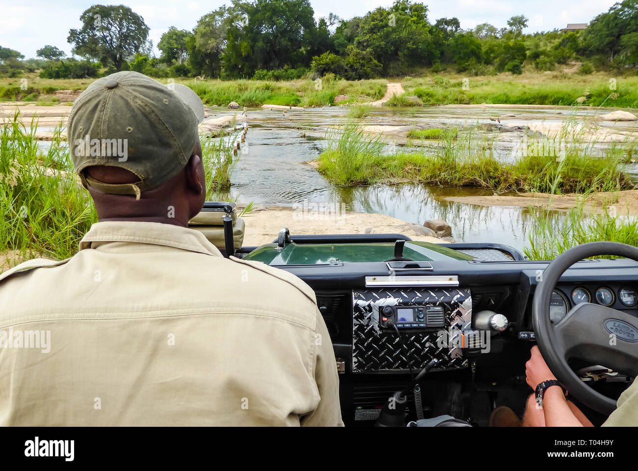 Hombre Negro tracker sentado en Safari Land Rover Defender vehículo de safari de cruzar el río en bush africano, Sabi Sands Game Reserve, Sudáfrica Foto de stock