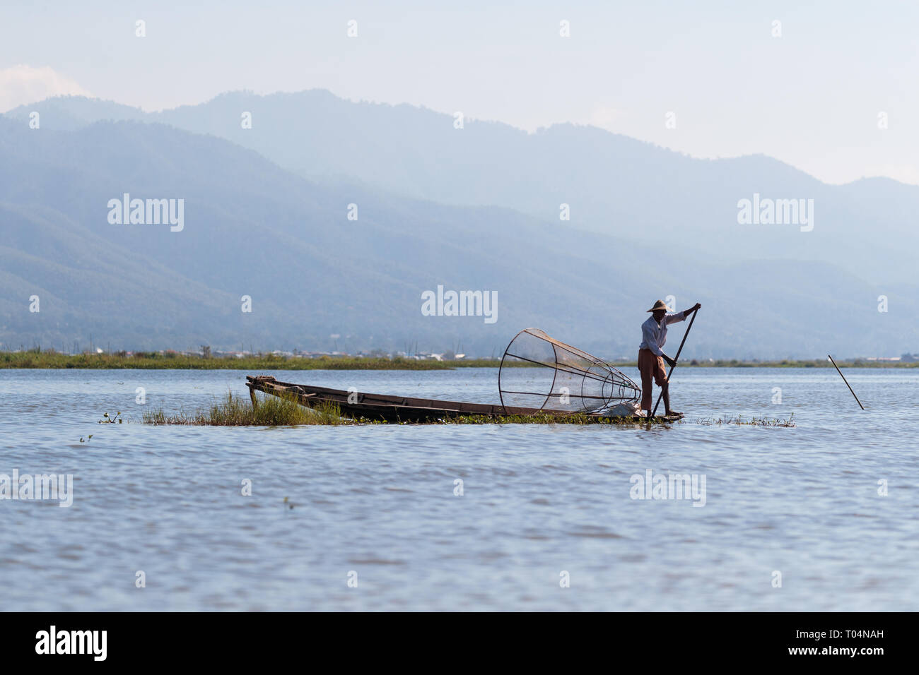 Los pescadores de pesca con Big Red en un único y tradicional estilo de remo de la pierna durante la puesta de sol sobre el Lago Inle en el estado de Shan, en Myanmar, Birmania Foto de stock