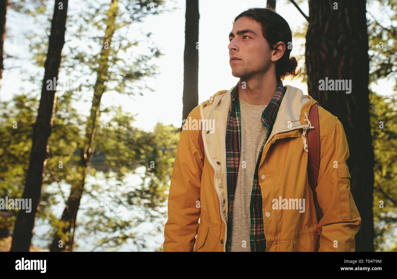 Hombre en un viaje de aventura en un bosque de pie mirando a otro lado. Retrato de un joven hombre vestido con chaqueta de explorar la naturaleza. Foto de stock