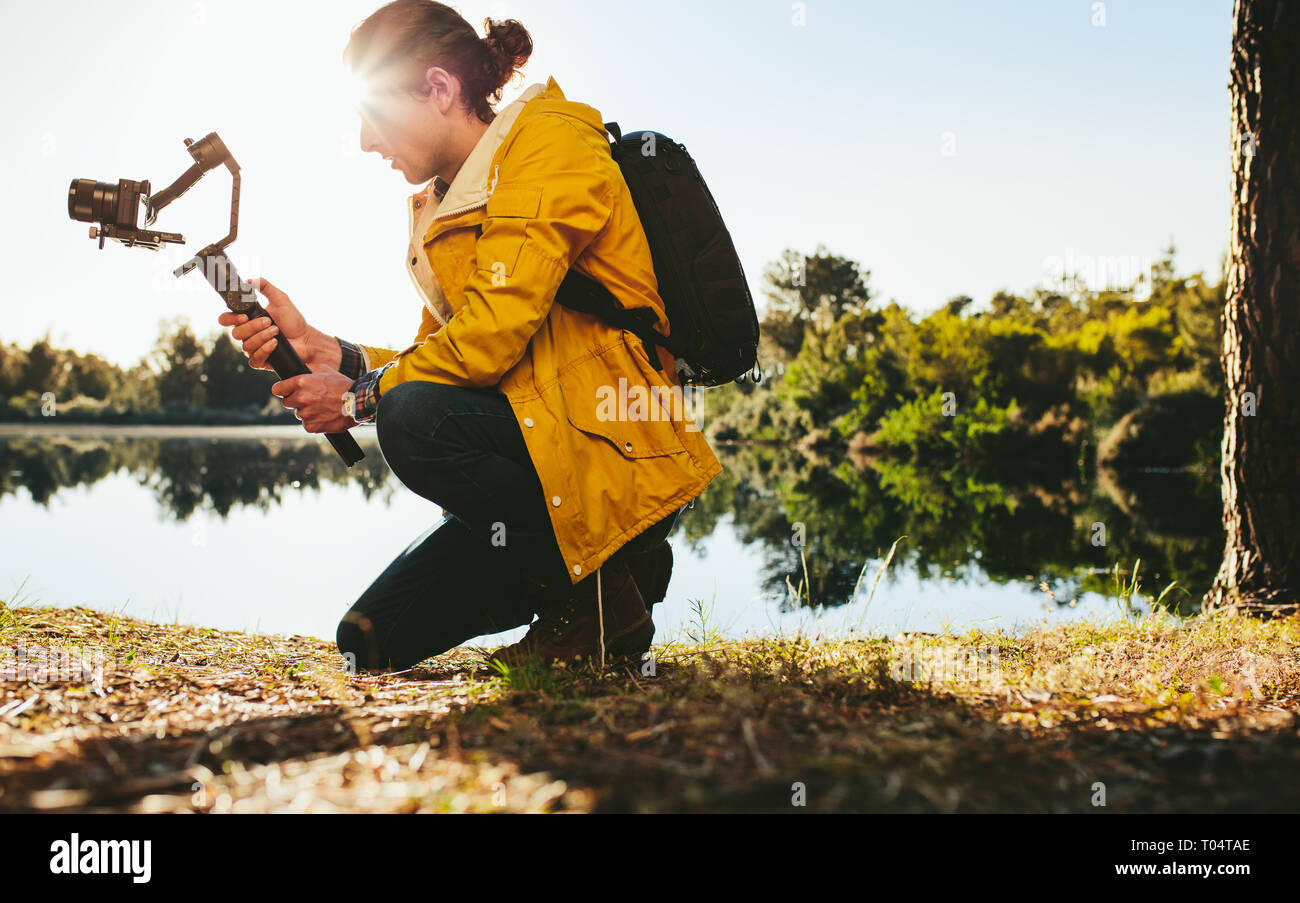 Hombre utilizando la avanzada tecnología gadgets para tomar fotografías de la naturaleza. Viajero sentado junto a un lago, tomando una fotografía en una cámara DSLR montada sobre una mano Foto de stock
