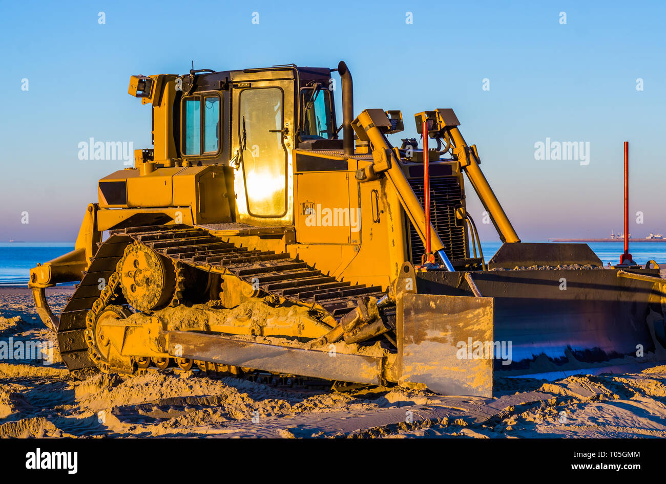 Vista lateral de un bulldozer con una boca en la playa, tierra de mover