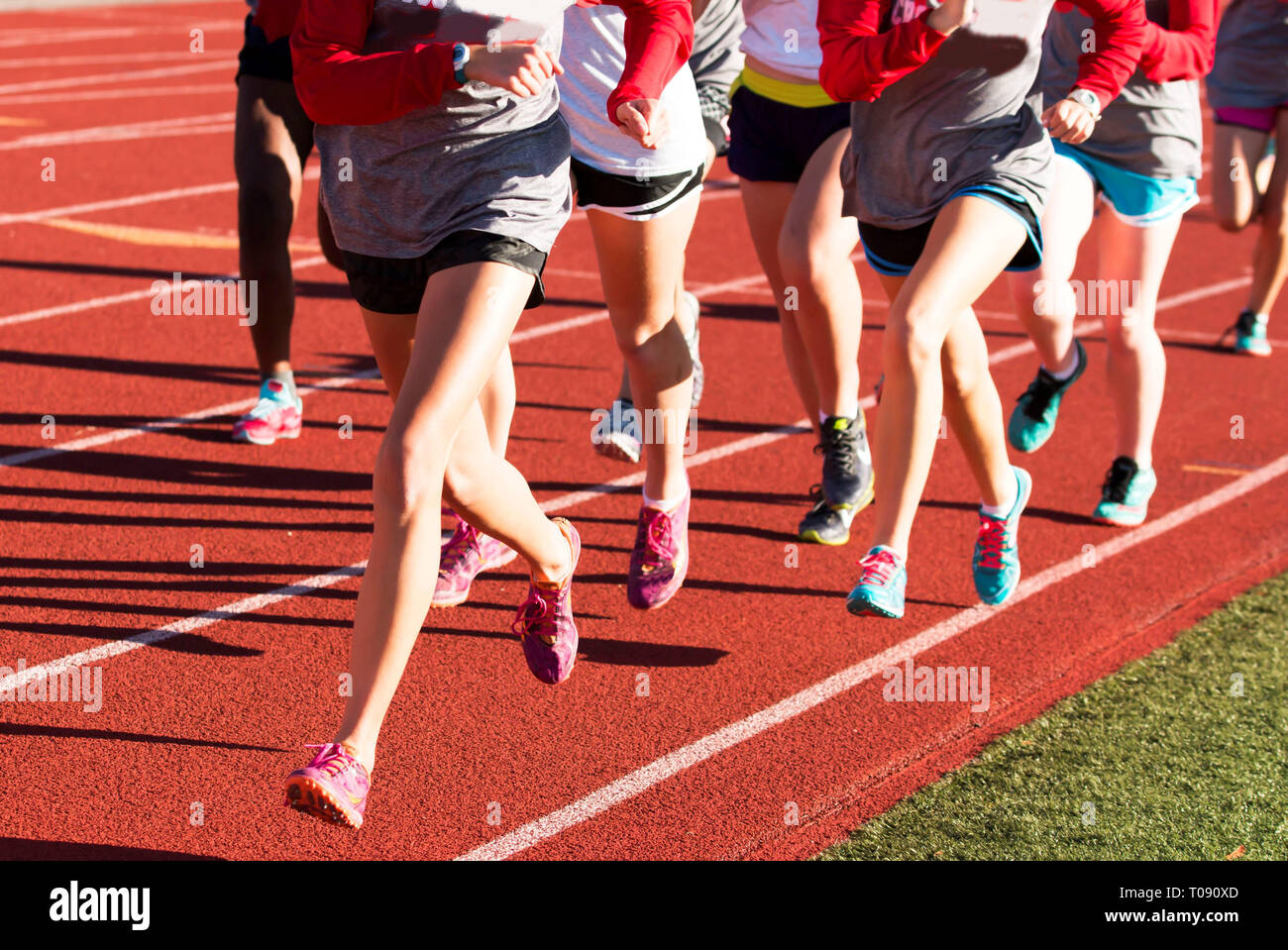 Las niñas cross country entrenar los intervalos de carrera juntos en una pista roja mientras llevaba picos. Foto de stock
