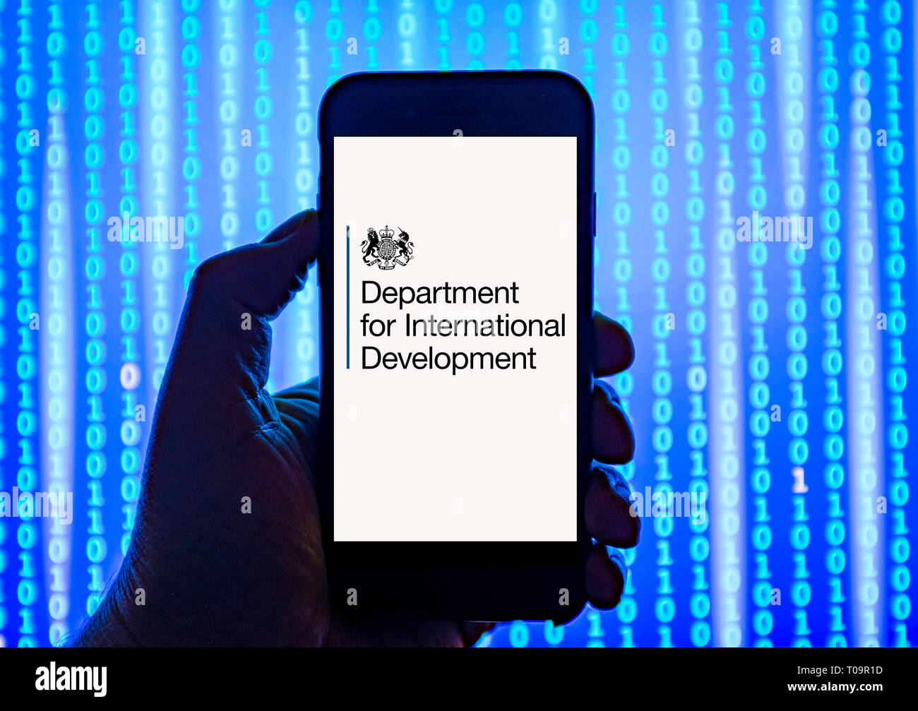 Persona sosteniendo el teléfono inteligente con el Departamento para el Desarrollo Internacional Logotipo mostrado en la pantalla. Foto de stock