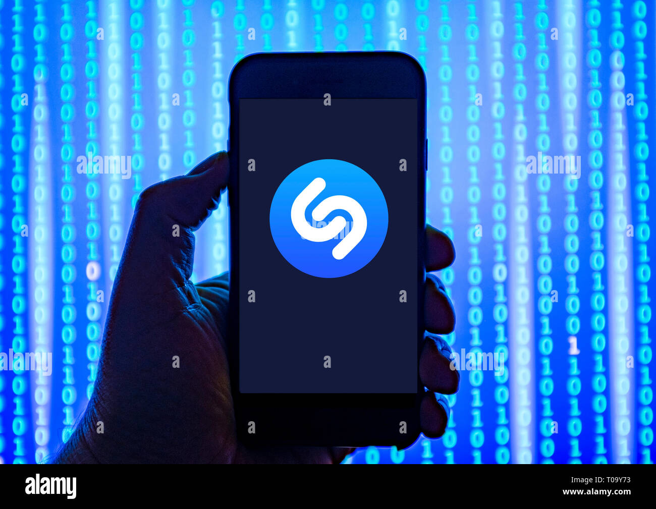 Persona sosteniendo el teléfono inteligente con reconocimiento de música Shazam online app logotipo mostrado en la pantalla. Foto de stock