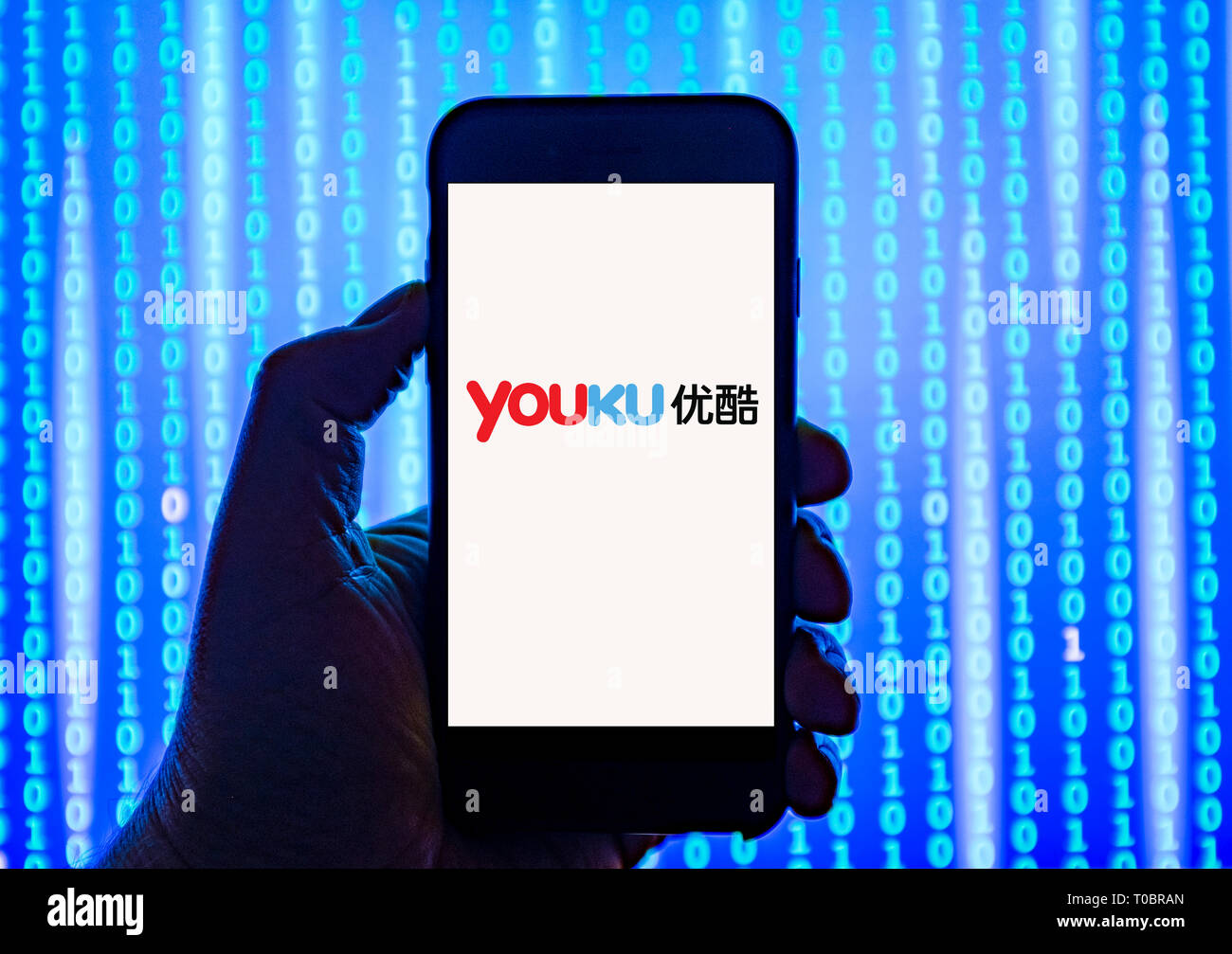Persona sosteniendo el teléfono inteligente con YouKu Logotipo mostrado en la pantalla. Youku Tudou Inc., haciendo negocios como youku, es un servicio de alojamiento de vídeo basado en Foto de stock