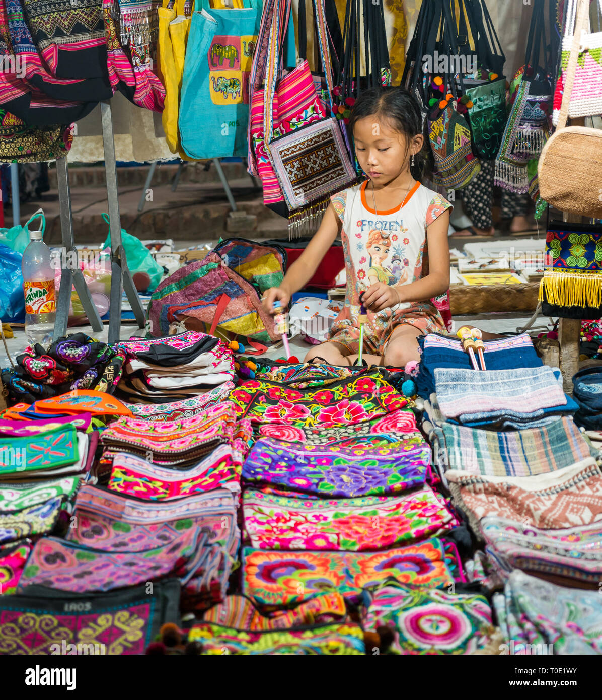 Chica joven jugando mientras minding souvenir puesto en el mercado nocturno turístico, Luang Prabang, Laos, se Asia Foto de stock