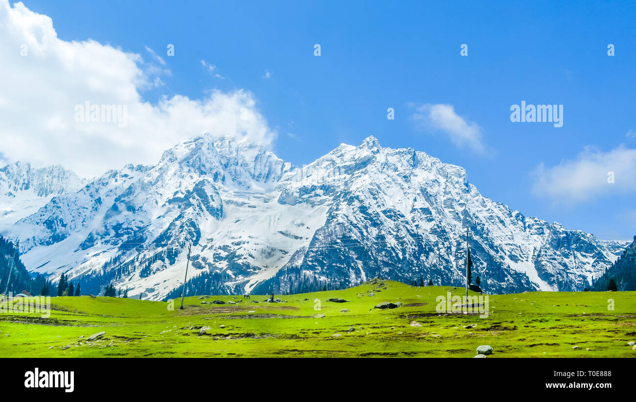 Amplia vista panorámica de picos de montañas cubiertos de nieve y el cielo azul con nubes en el valle Baisaran Mini (Suiza), Pahalgam, Cachemira, India Foto de stock