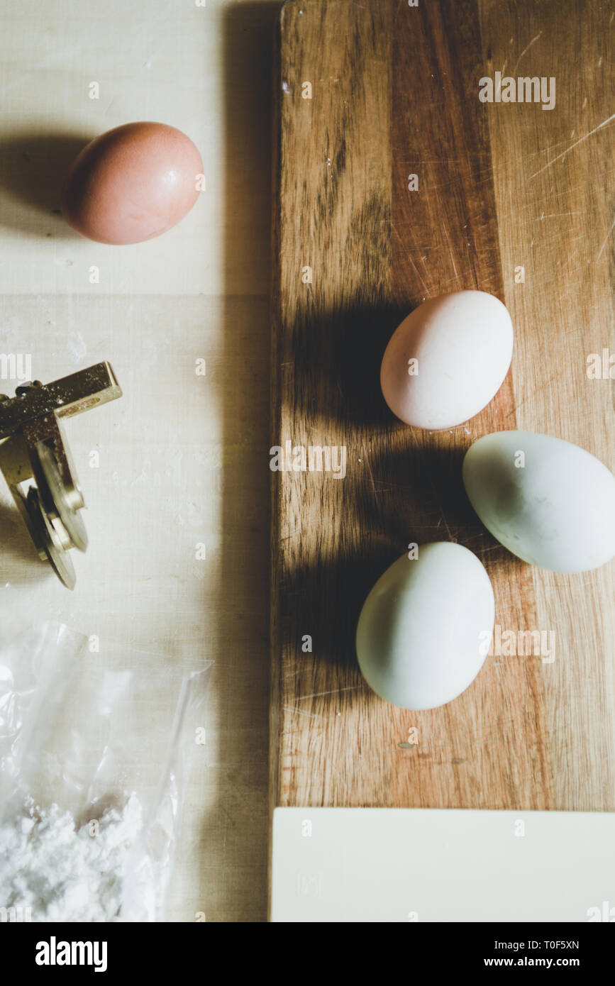 Hacer la pasta en casa, natural de huevo verde oliva, Egger, blanco y marrón, huevo, harina y pasta cutter sobre un fondo de madera Foto de stock