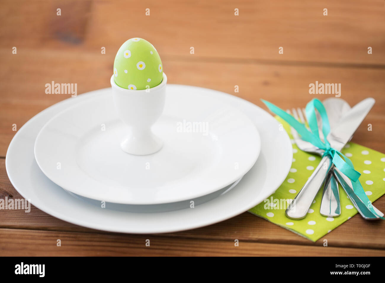 Huevo de pascua en el portavasos, platos y cubiertos. Foto de stock
