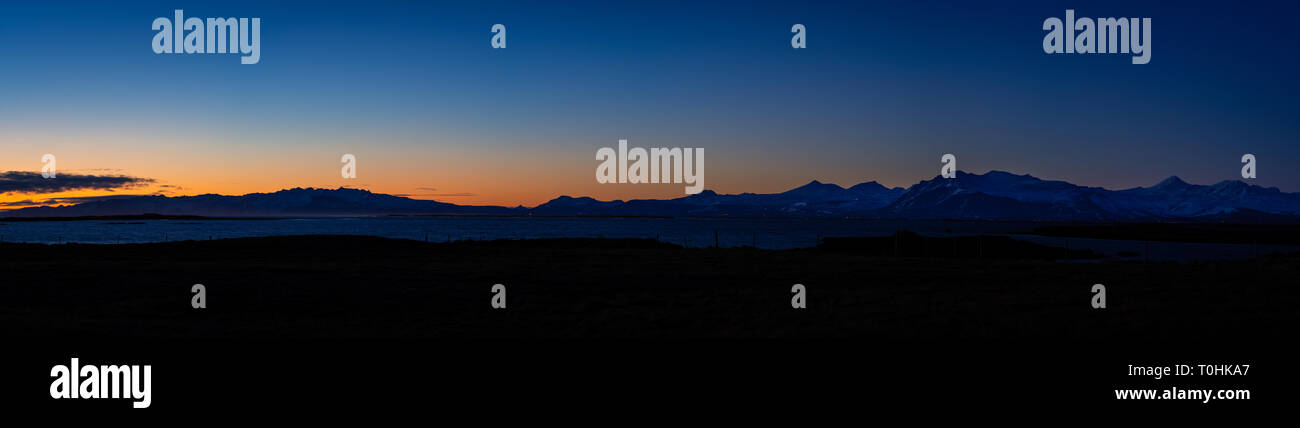 Vista panorámica de la puesta del sol sobre el oeste de Islandia. Lejos del sol por debajo del horizonte, creando una cordillera silueta en el intenso azul del cielo. Foto de stock