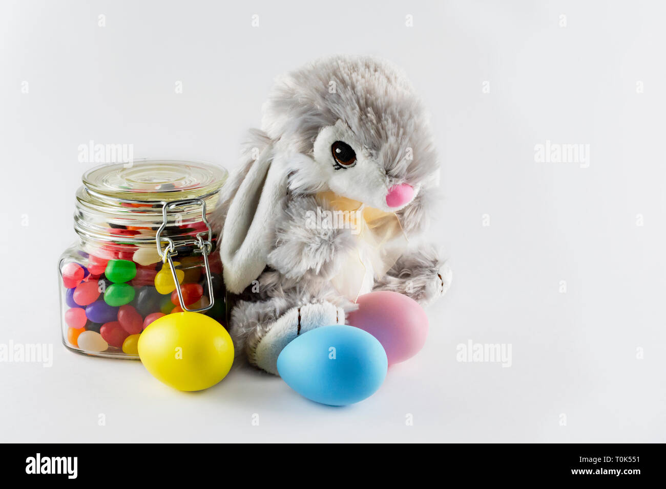 Peluche Conejo de pascua con coloridos teñido de huevos y un tarro de vidrio lleno de Jelly Beans sobre un fondo blanco. Copie el espacio a la derecha. Foto de stock