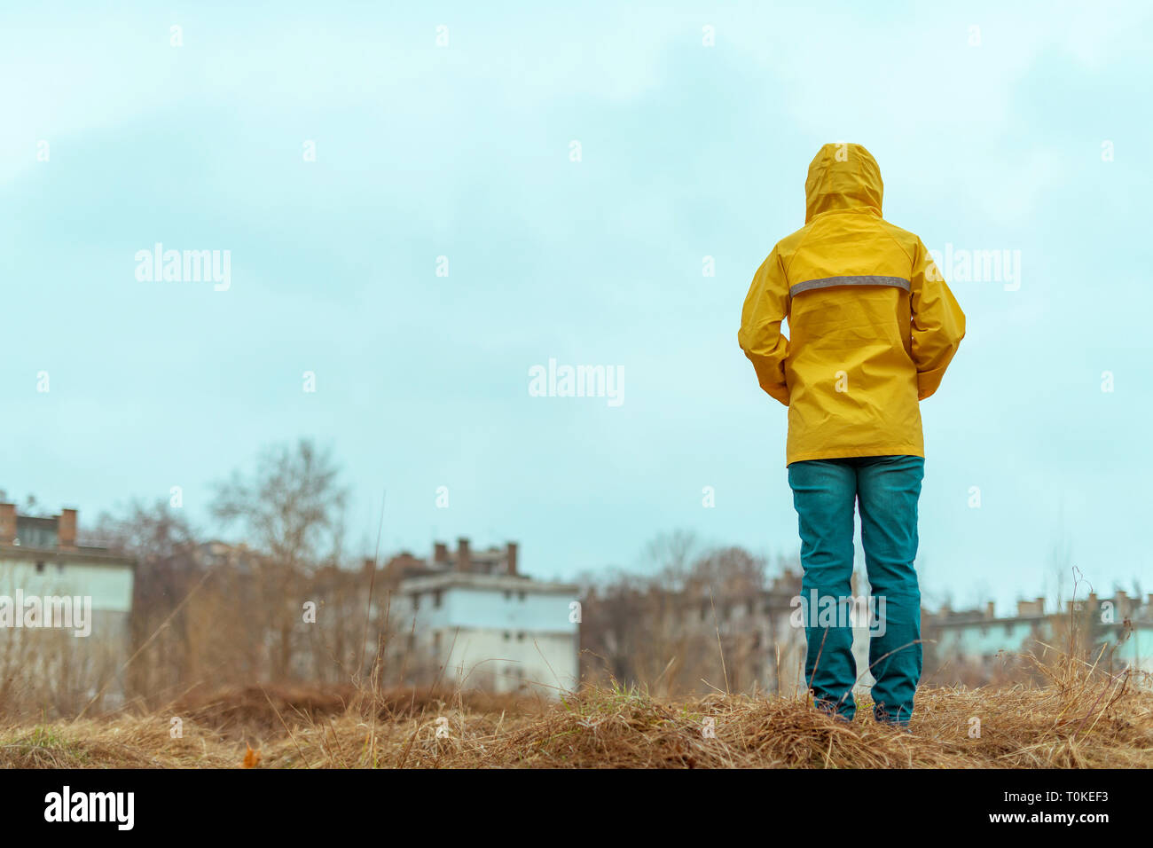 Vista trasera de la mujer en impermeable mirando a distancia en invierno lluvioso día nublado Foto de stock