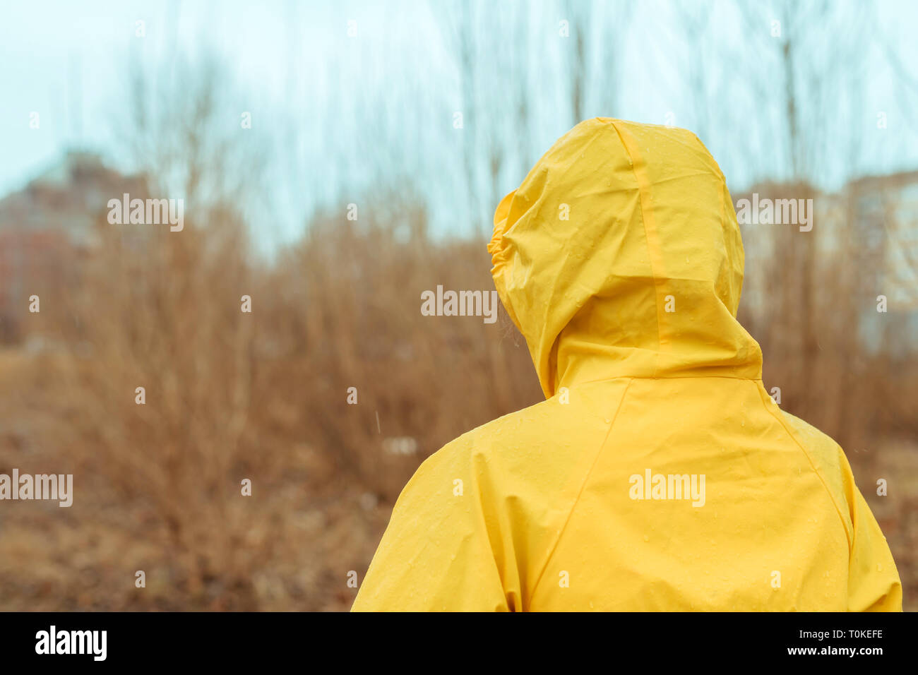 Vista trasera de la mujer en impermeable mirando a distancia en invierno lluvioso día nublado Foto de stock