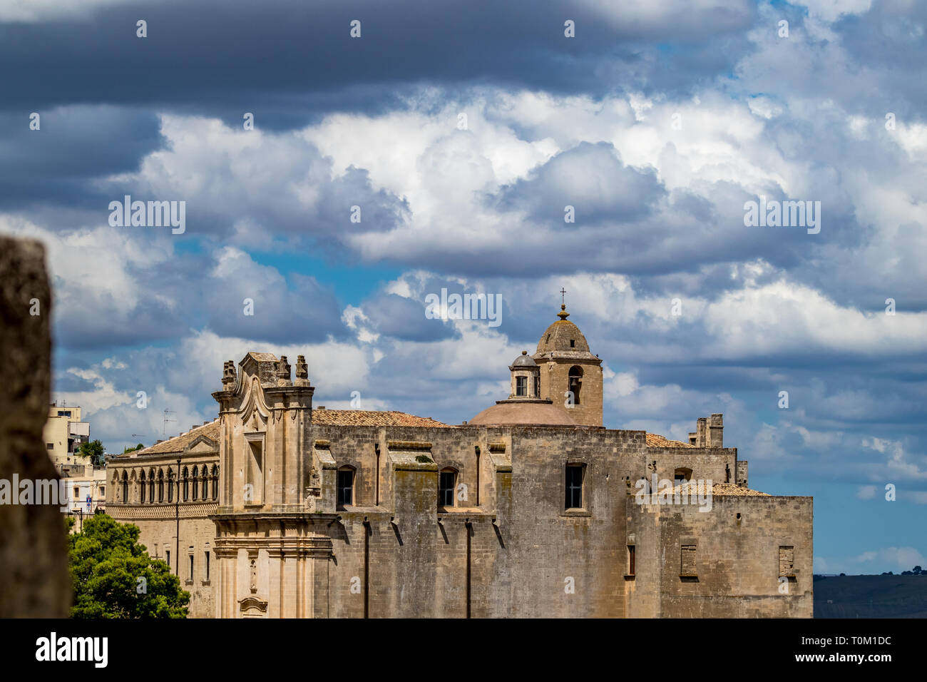 La torre de la iglesia y el techo con religioso cruz de Chiesa di Sant'Agostino, vista de la antigua ciudad de Matera, Basilicata, en el sur de Italia, nublado verano cálido Foto de stock