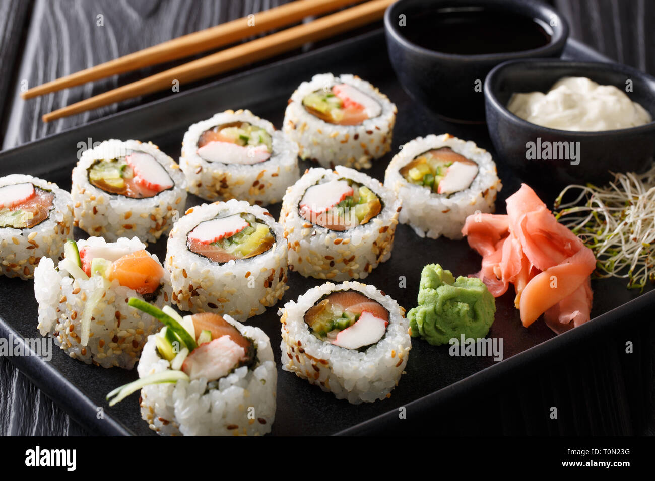 Conjunto de rodillos Uramaki servidos con salsas, brotes de soja, jengibre y wasabi closeup en una placa horizontal sobre la mesa. Foto de stock