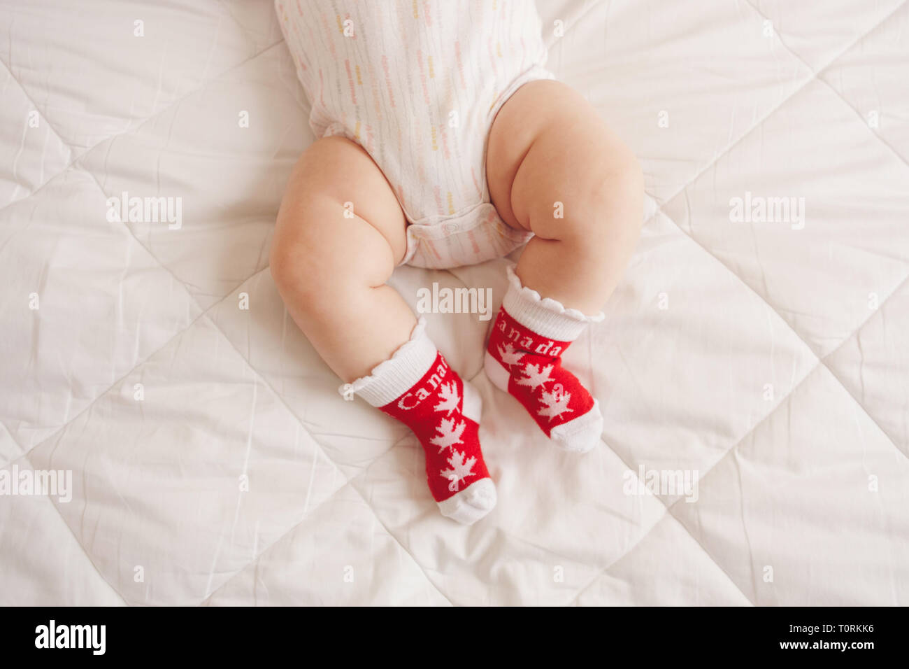 Acercamiento del bebé gordito blanco pies piernas vistiendo calcetines rojos  con el Canadian Maple Leaf flag. Niño bebé acostado en la cama en ropa con  símbolo nacional de C Fotografía de stock -