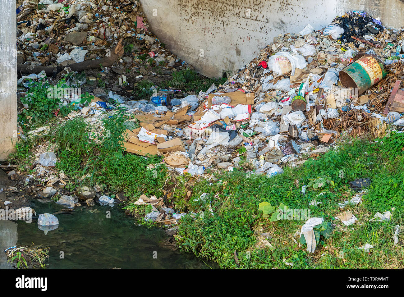 Residuos de basura al lado de un río, bajo un puente Foto de stock