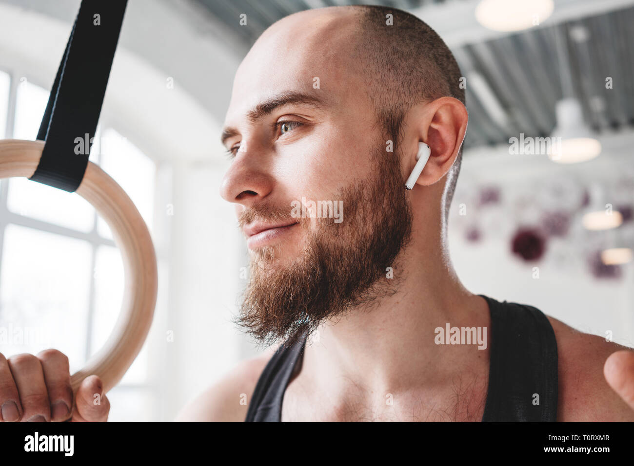Retrato atleta masculino barbado usando auriculares inalámbricos en la sala  de deportes. Colocar sonriente hombre sujetando el gimnasta anillos y mirar  lejos Fotografía de stock - Alamy