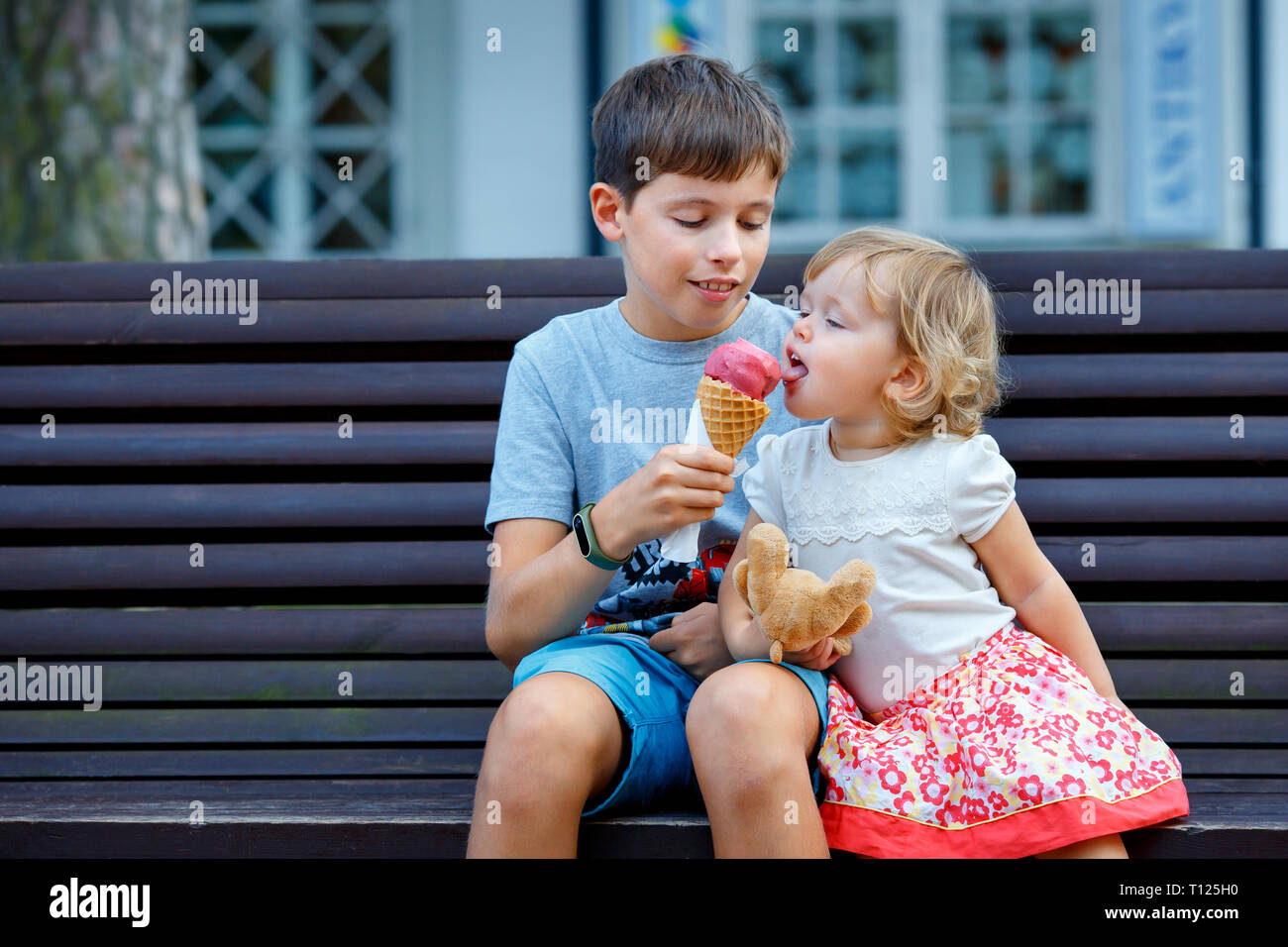 Gran hermano dando su helado a hermana pequeña piscina Foto de stock