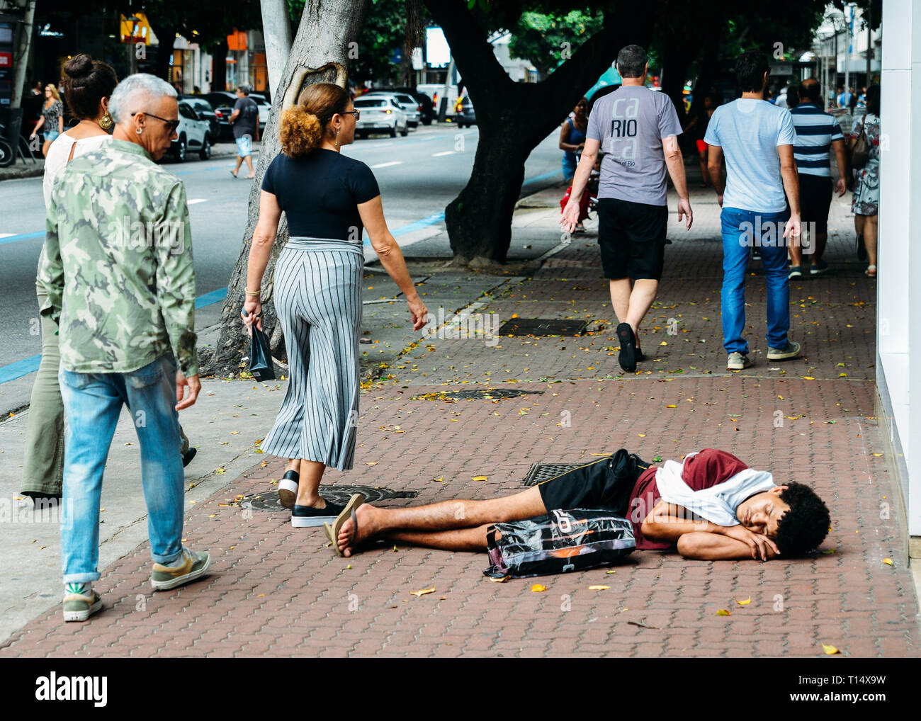Río de Janeiro, Brasil, 23 de marzo de 2019: el joven sin hogar durmiendo mientras los peatones caminar junto a él en la concurrida acera peatonal en la riqueza Foto de stock