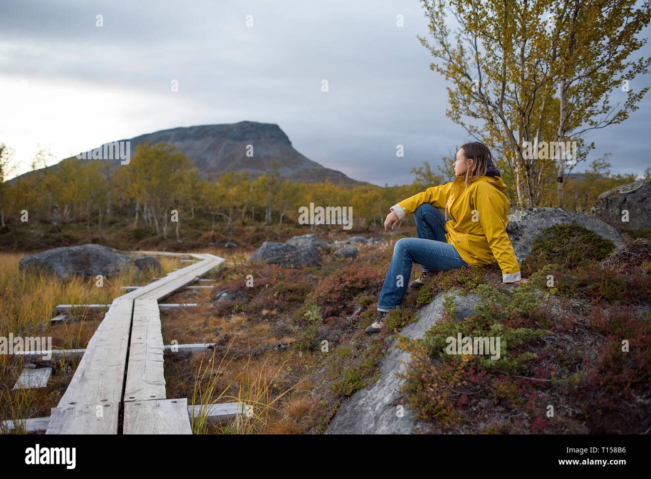 Finlandia, Laponia, Kilpisjaervi, mujer sentada en el paseo marítimo de madera Foto de stock