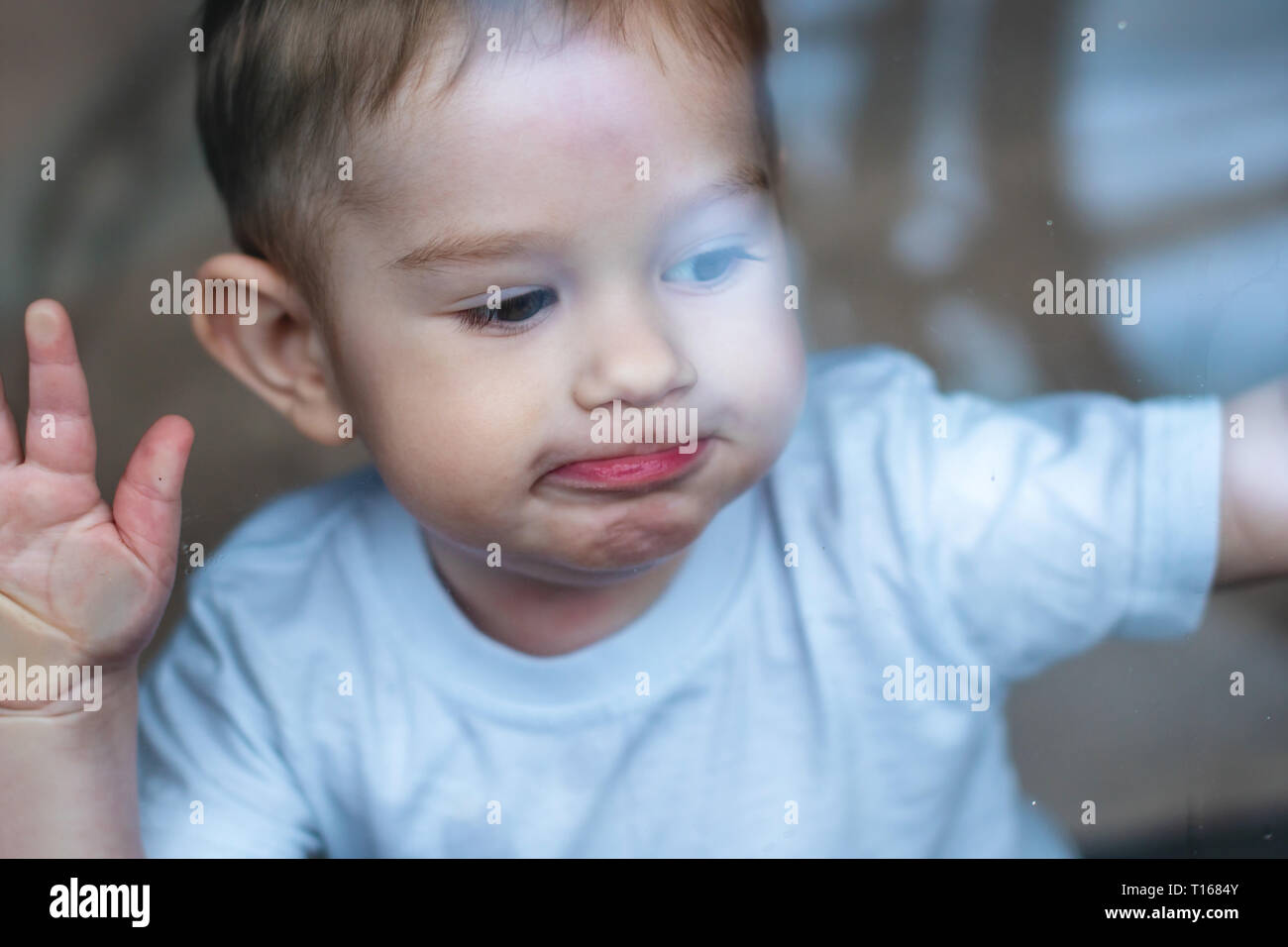 Hermoso lindo bebé niño mirando en el cristal de la ventana con la reflexión. El concepto de la soledad de los niños y espera de amabilidad. Orfanato y orp de stock -