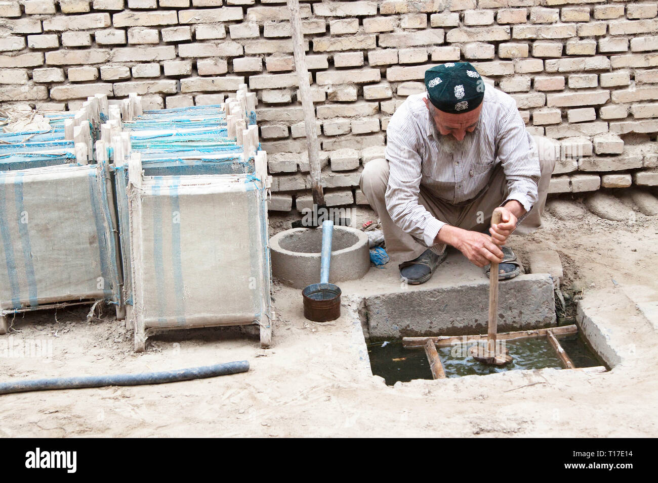 Viejo hombre uigur mezcla de corteza de morera ' sopa preparada para hacer las hojas de morera de corteza triturada. Tradicionales de fabricación de papel de morera, Hotan,, Xinjian Foto de stock