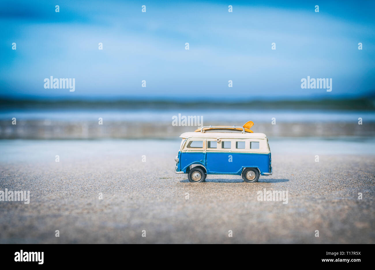 Vintage pequeña autocaravana juguete amarillo con placas de surf en la playa de arena con olas borrosas en segundo plano. Foto de stock