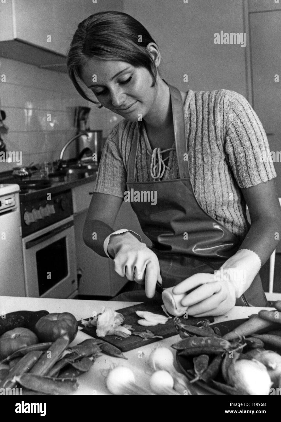 Hogar, cocinar y hornear, joven cortando vegetal con guantes de goma por 'Mapa', circa 1970, Additional-Rights-Clearance-Info-Not-Available Foto de stock