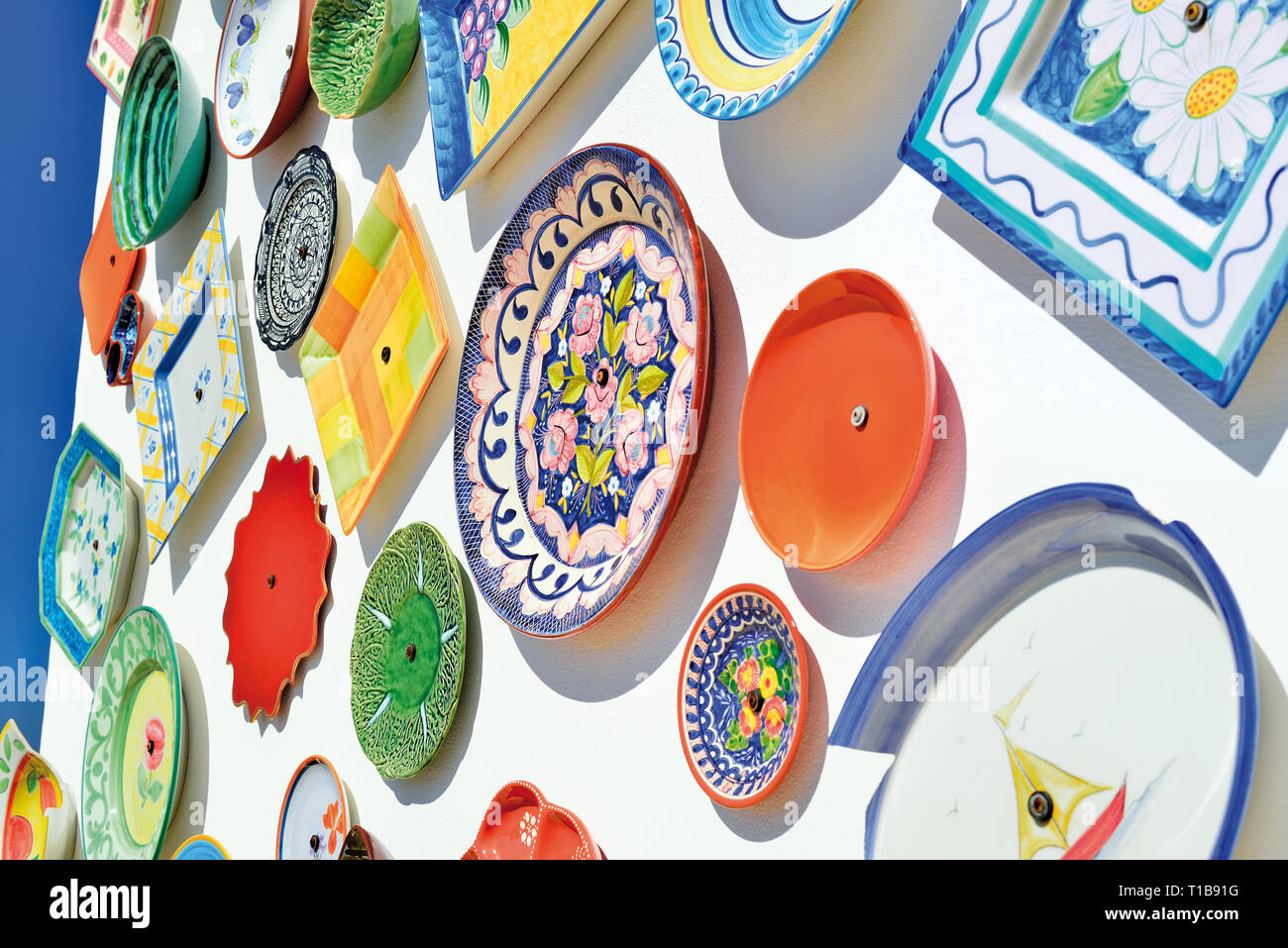 Placas cerámicas multicolores sobre una pared blanca lavada en un día soleado con el cielo azul Foto de stock