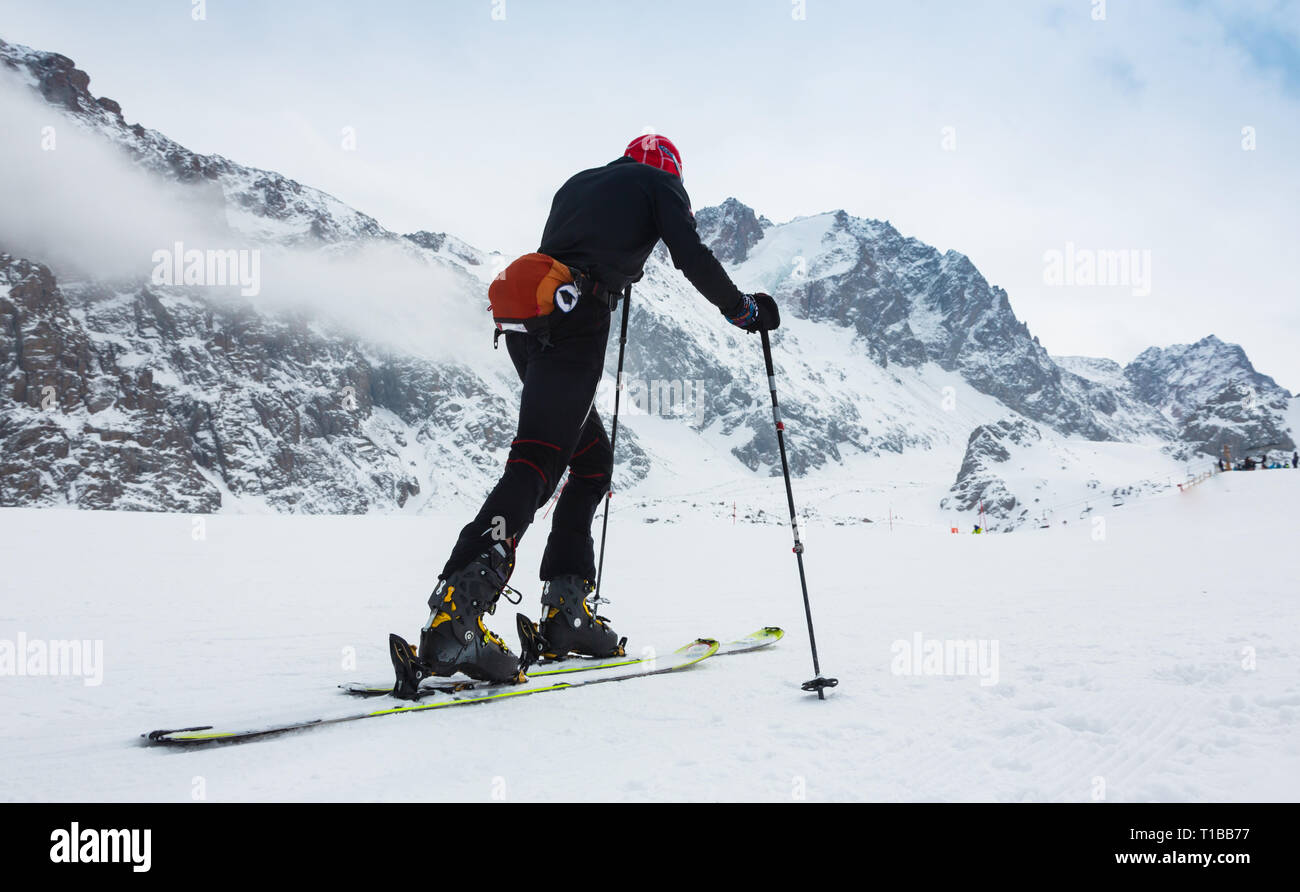 Esquí de travesía alpinista subiendo a lo largo de una cresta de nieve con esquís en la mochila. En el fondo azul del cielo y el brillante sol y Zebru, Ortler en el sur Foto de stock