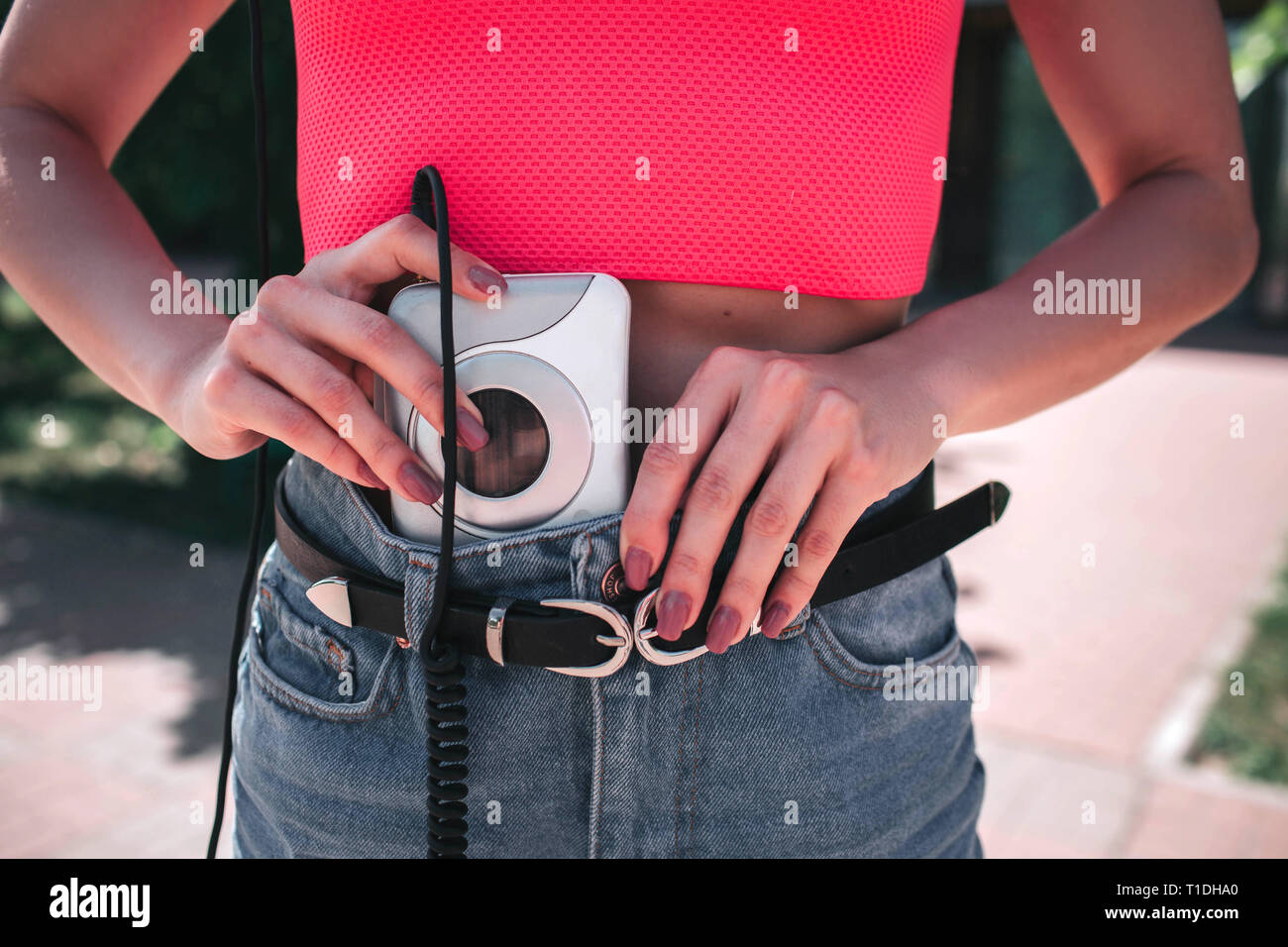 Una imagen de chica poniendo music player en pantalones vaqueros. Es blanca y reproductor de música a los auriculares conectados por cable. Foto de stock