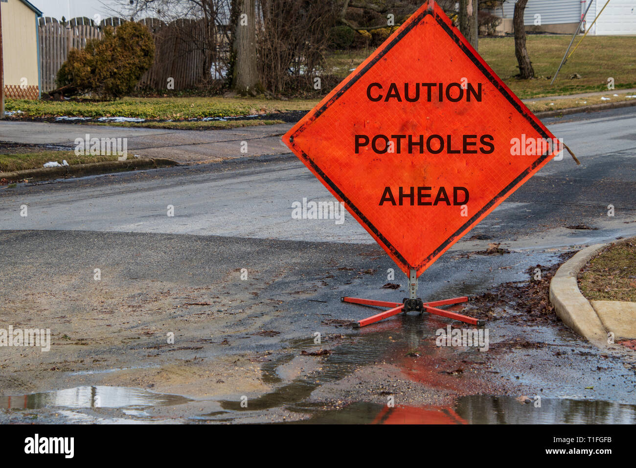 Señal de tráfico triangular naranja sobre una pequeña calle suburbana