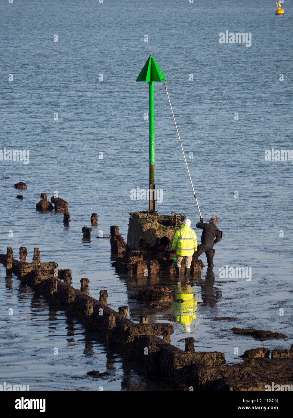 Par de dos trabajadores hombres trabajadores en alta vis trabajando manteniendo la pintura repintado con pértiga Rodillo del cepillo una playa espigón navegación marcadores Foto de stock