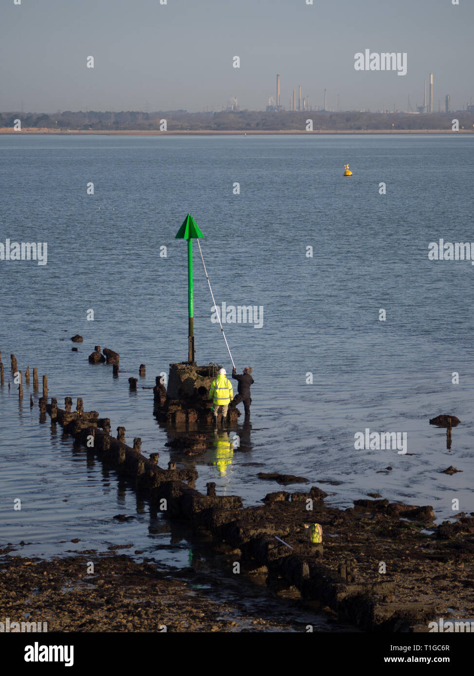 Par de dos trabajadores hombres trabajadores en alta vis trabajando manteniendo la pintura repintado con pértiga Rodillo del cepillo una playa espigón navegación marcadores Foto de stock