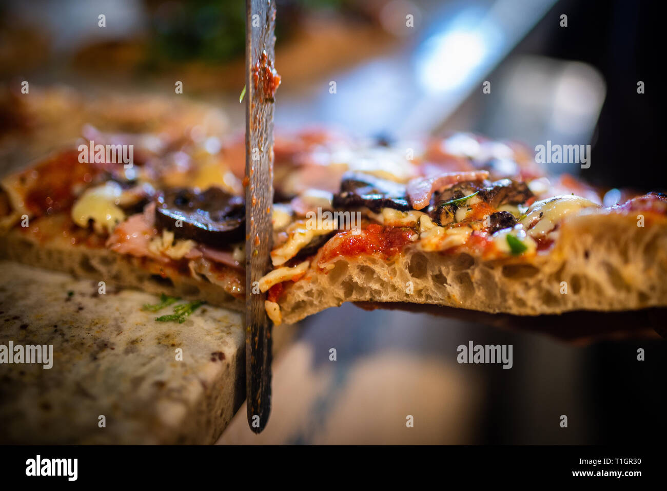 Una rodaja de estilo romano tradicional pizza de leña cortarse con un cuchillo en una pizzería italiana/trattoria/restaurante. Enfoque selectivo Foto de stock