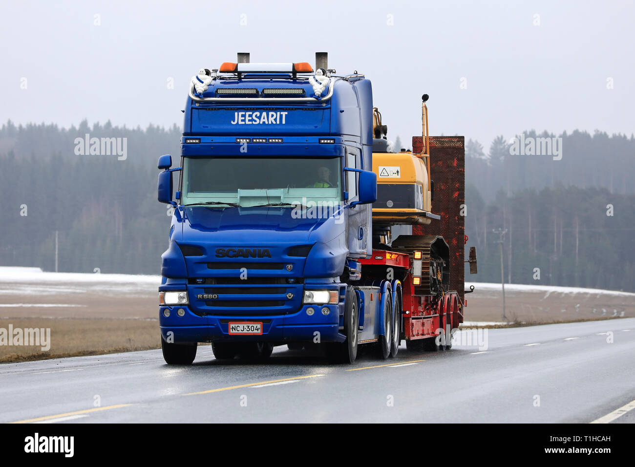 Jokioinen, Finlandia - 23 de marzo de 2019: Azul Scania R580 Cabina convencional de Maansiirto Jeesarit Oy lances excavadora orugas en el remolque por la carretera. Foto de stock