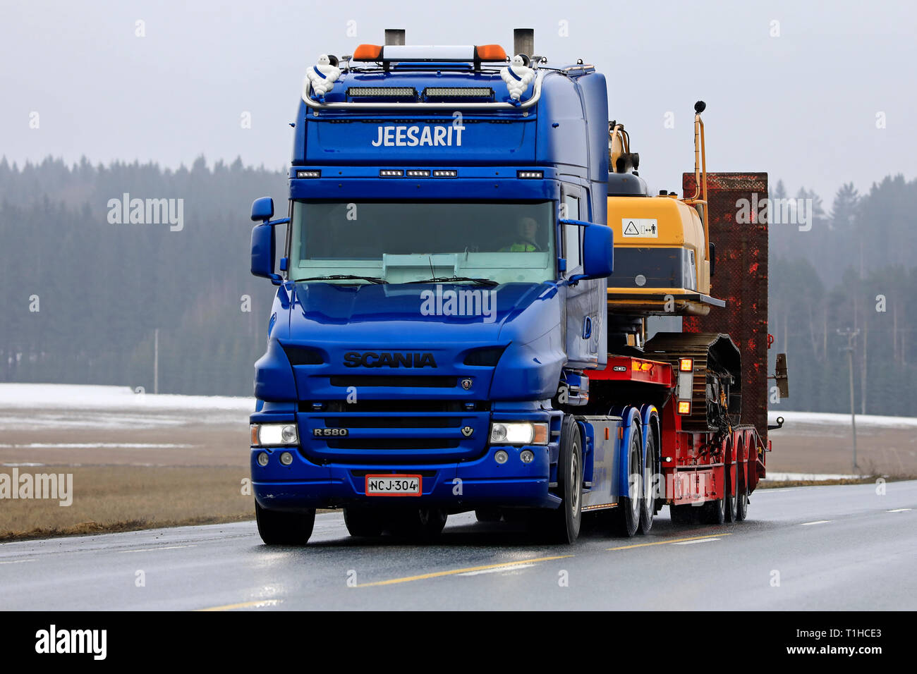 Jokioinen, Finlandia - 23 de marzo de 2019: Azul Scania R580 Cabina convencional de Maansiirto Jeesarit Oy lances excavadora orugas en el remolque por la carretera. Foto de stock