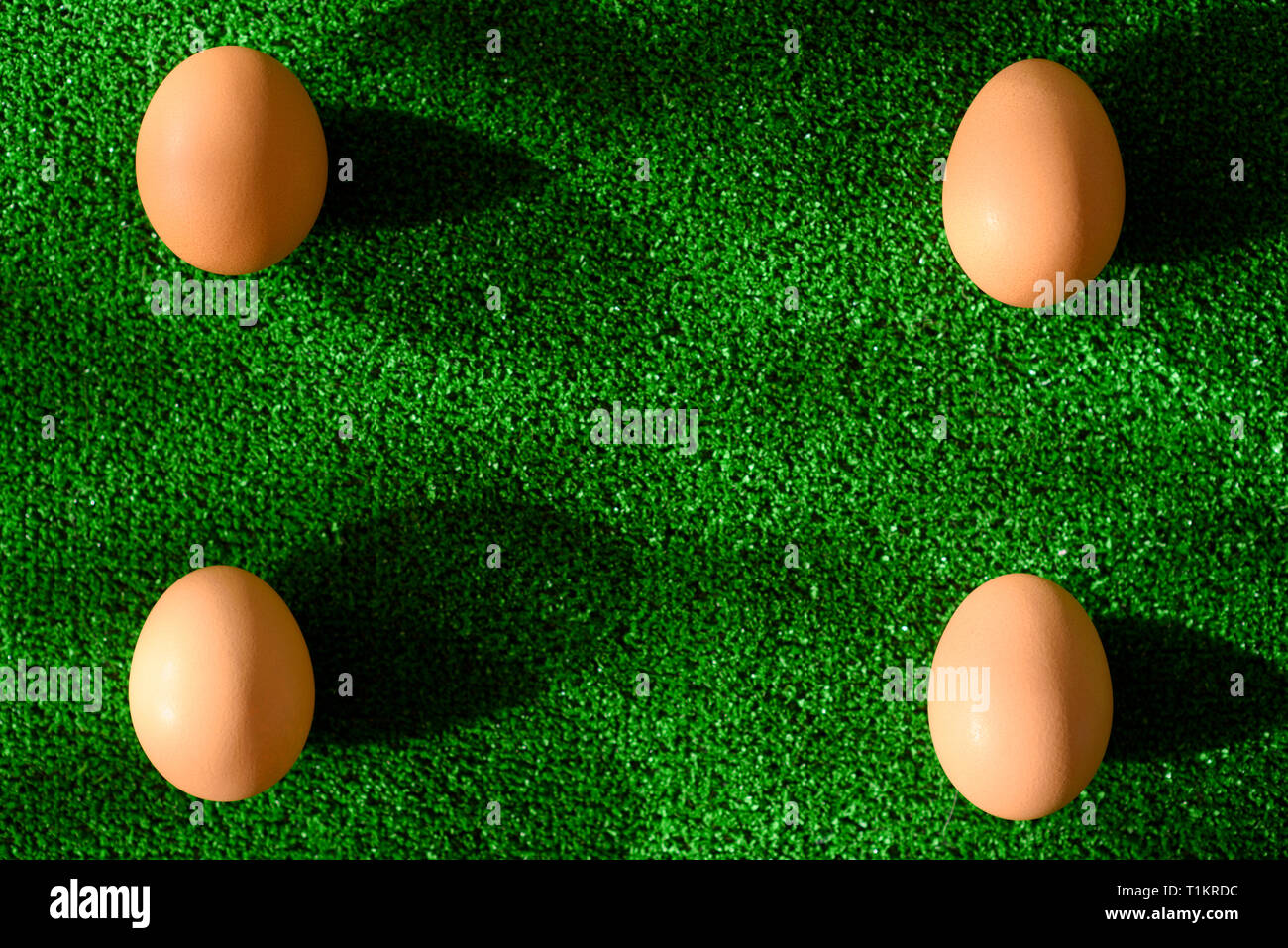 Vista superior de cuatro huevos en las cuatro esquinas, sobre fondo de hierba verde, con copia espacio en el medio. Foto de stock