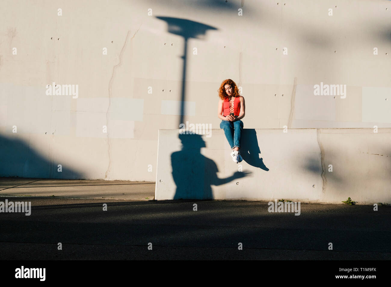 Sombra mirando a una mujer joven usando un teléfono inteligente en la pared urbana Foto de stock