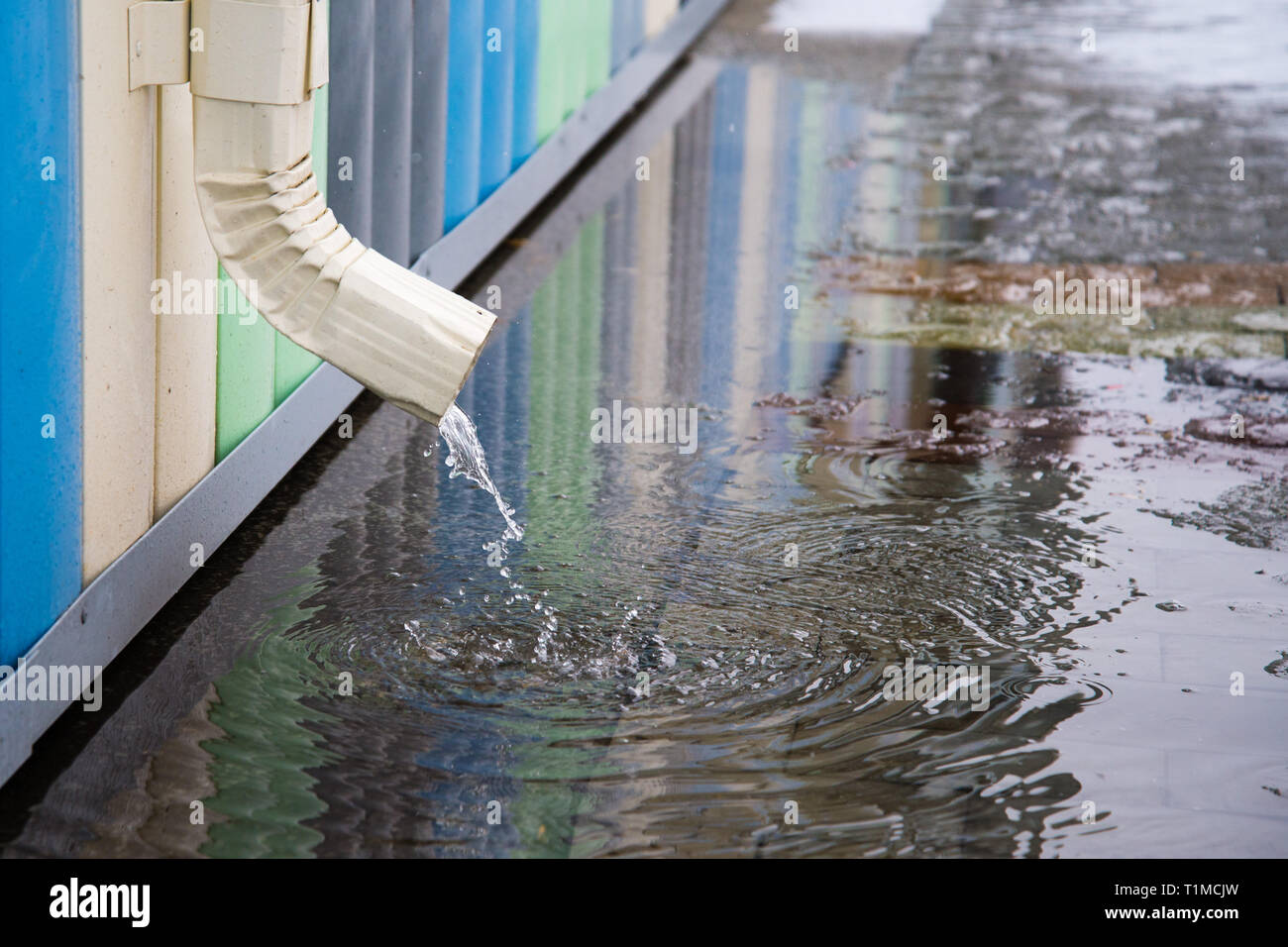Desagüe blanco con pavimento inundadas. El agua de lluvia que fluye desde el tubo de desagüe closeup. Foto de stock