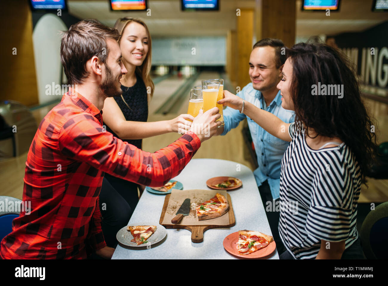 Amigos bebidas y come pizza en Bowling Club Foto de stock