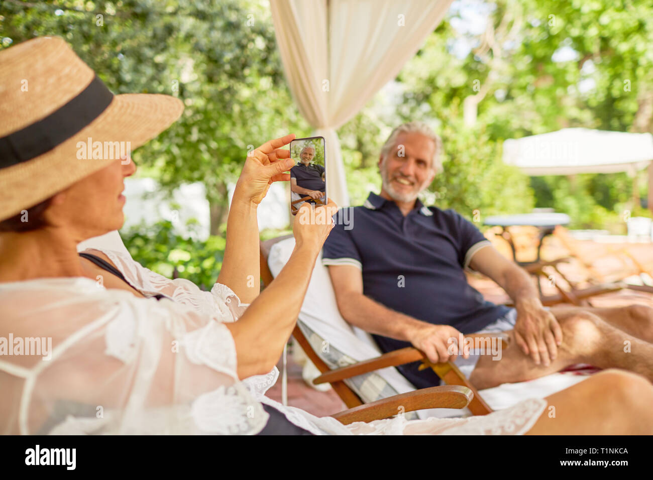 Esposa con teléfono con cámara de fotografiar el marido en el resort piscina. Foto de stock