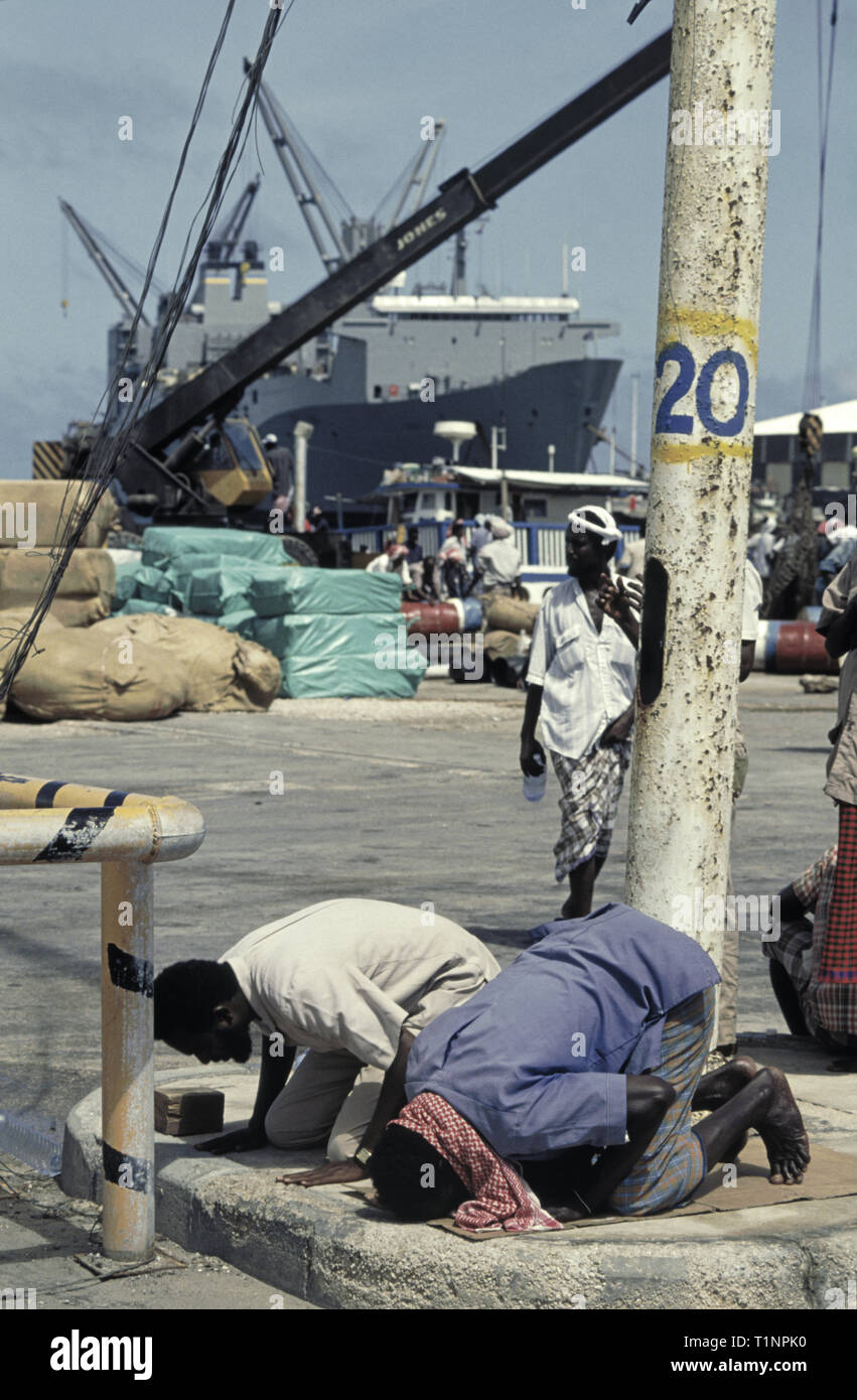 29th de octubre de 1993 Hombres somalíes rezan hacia la Meca en el nuevo puerto de Mogadishu, Somalia. En el fondo está el enorme buque de carga de vehículos de la Administración Marina de los Estados Unidos, USNS Denebola. Foto de stock