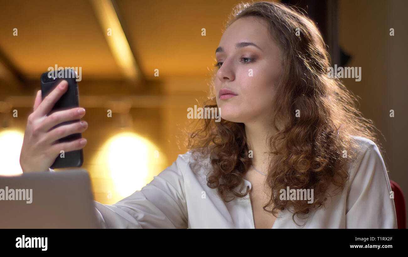 Retrato del joven empresaria selfie concentrada haciendo fotos usando el smartphone en el fondo de la oficina. Foto de stock