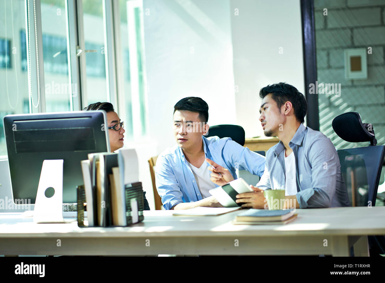 Tres jóvenes ejecutivos asiáticos trabajan juntos hablando de plan de negocios en la oficina. Foto de stock