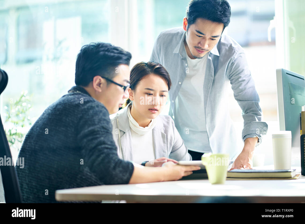 Tres jóvenes ejecutivos asiáticos trabajan juntos hablando de plan de negocios en la oficina. Foto de stock