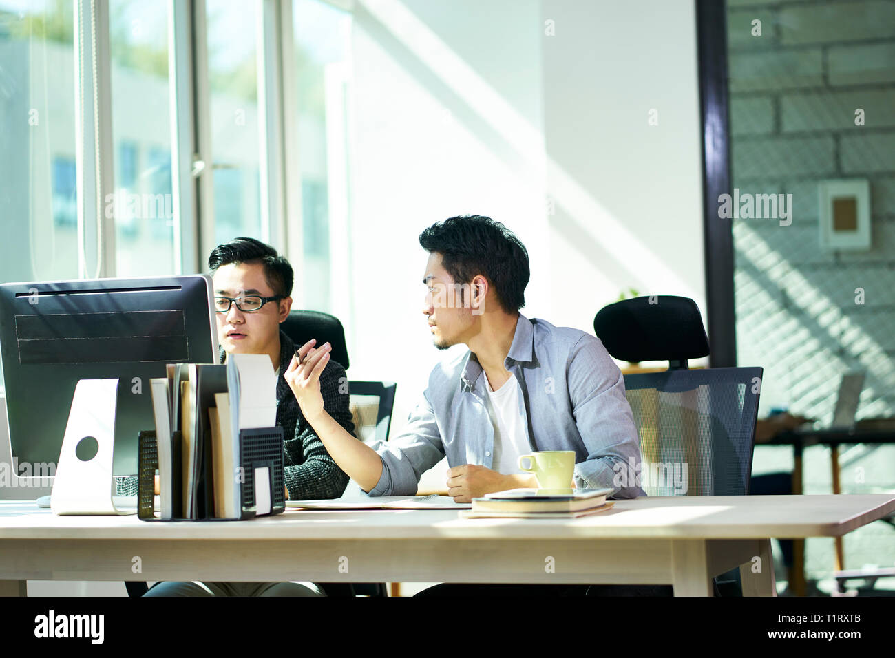 Dos jóvenes empresarios asiáticos trabajan juntos en la oficina hablando de negocios. Foto de stock