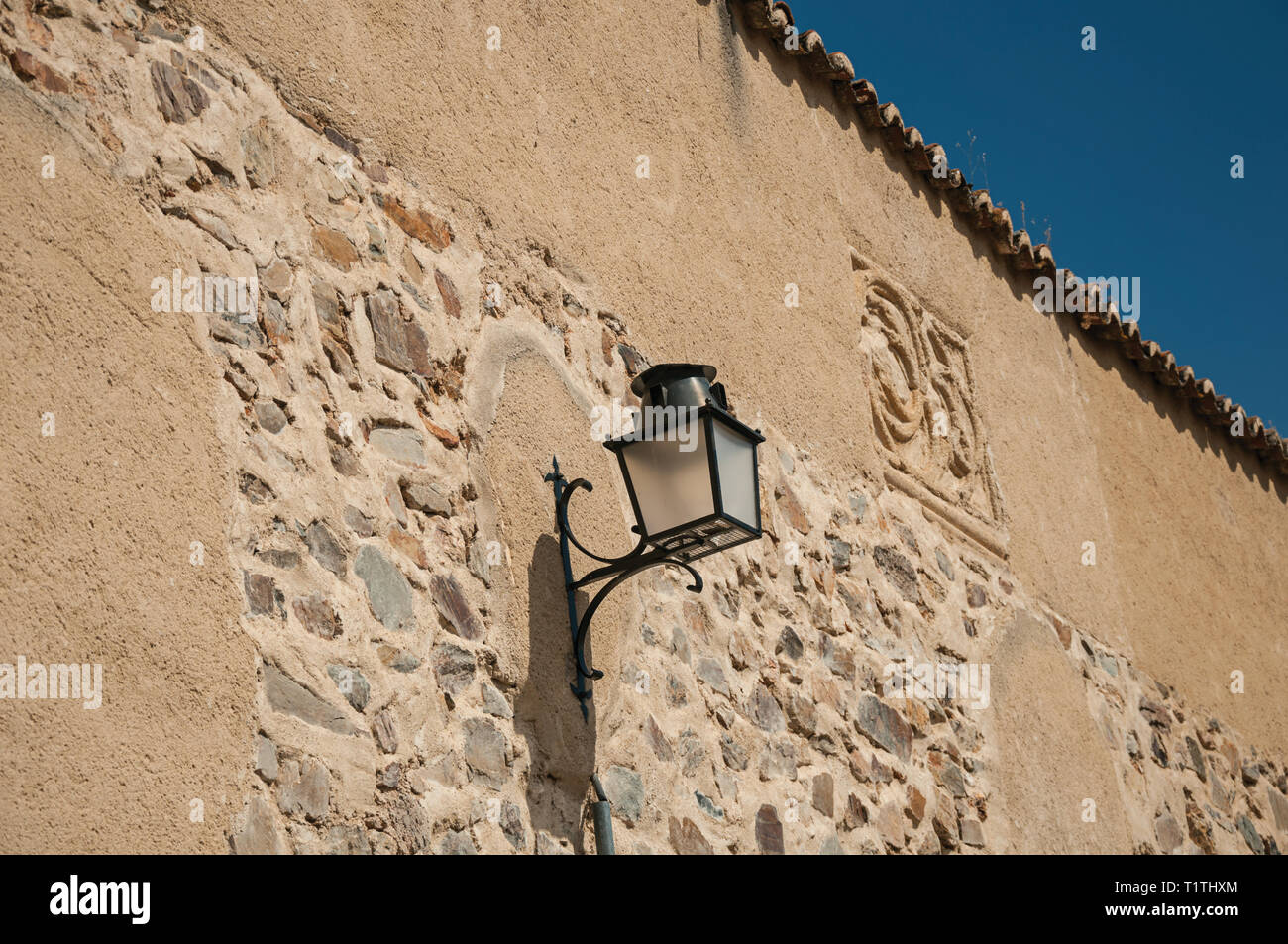 Viejo estilo candelabro de metal pegada a la pared de piedra y luz suave en  un callejón al atardecer en Caceres. Un pueblo lleno de edificios antiguos  en España Fotografía de stock -