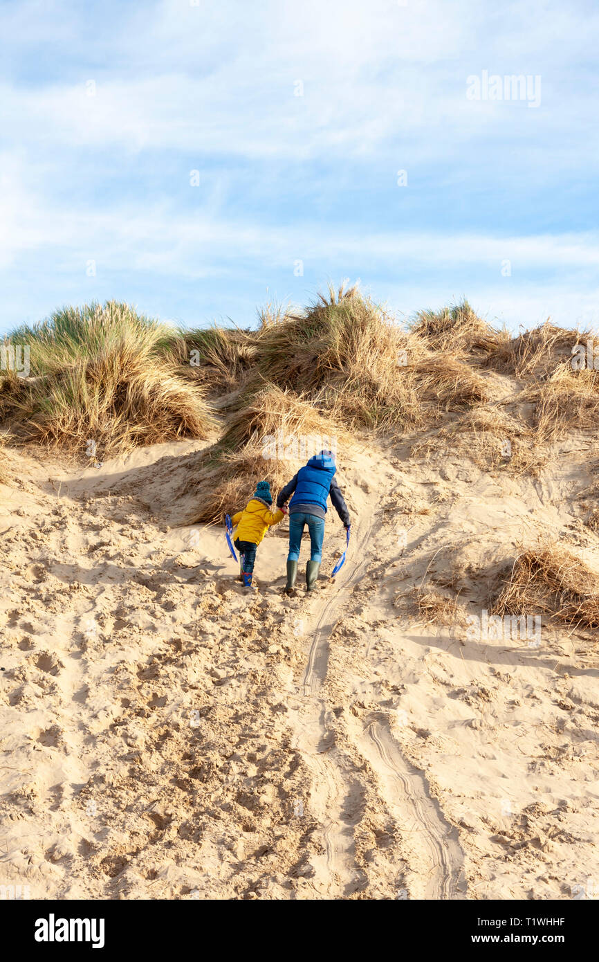 Un adulto y un niño subiendo por una duna de arena en la playa Formby, Merseyside, REINO UNIDO Foto de stock